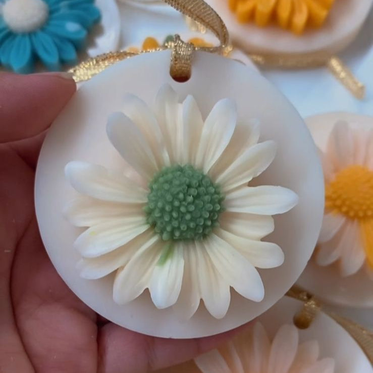 Hand holding a white flower-shaped object with other colorful flower-shaped objects in the background.